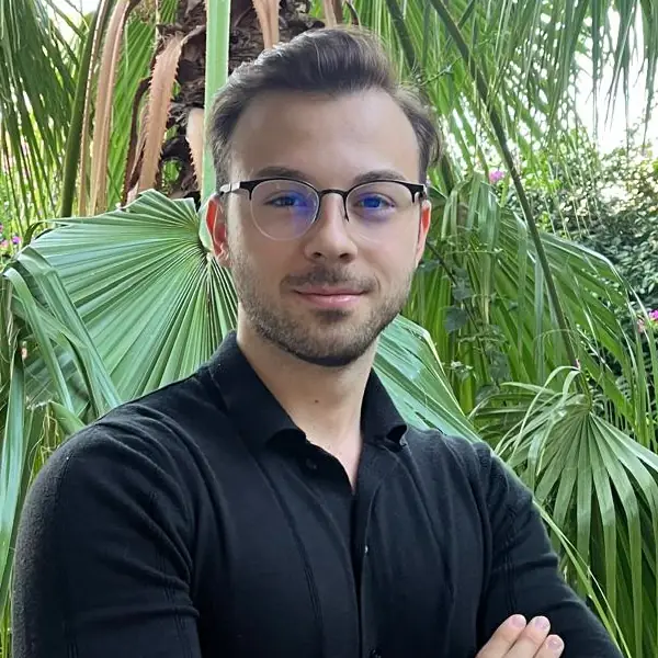 Diyetisyen Arman Ünsal, yeşil bitkilerin önünde kollarını kavuşturmuş halde